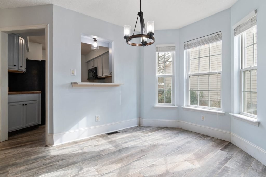 Sunlit empty room featuring a modern chandelier and wooden floors, ideal for home staging.